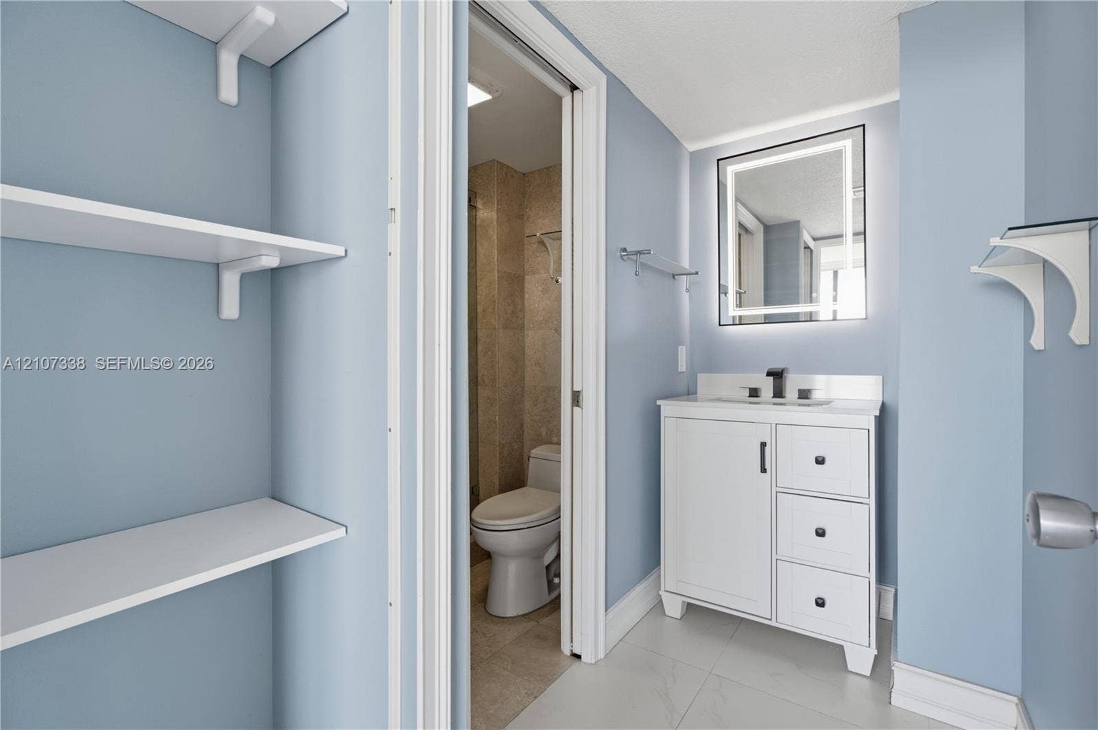 20355 NE 34th Court, #1824, Aventura, FL 33180 Vanity featuring a white cabinet with integrated drawers, stone countertop, matte black faucet, and an illuminated rectangular mirror