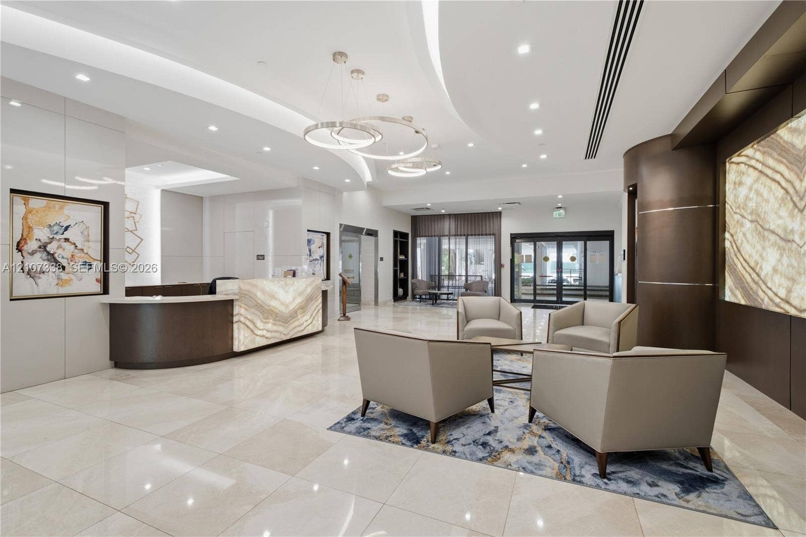 20355 NE 34th Court, #1824, Aventura, FL 33180 High-ceiling lobby featuring a backlit stone-front reception desk, polished stone flooring, recessed lighting, and contemporary ring chandeliers