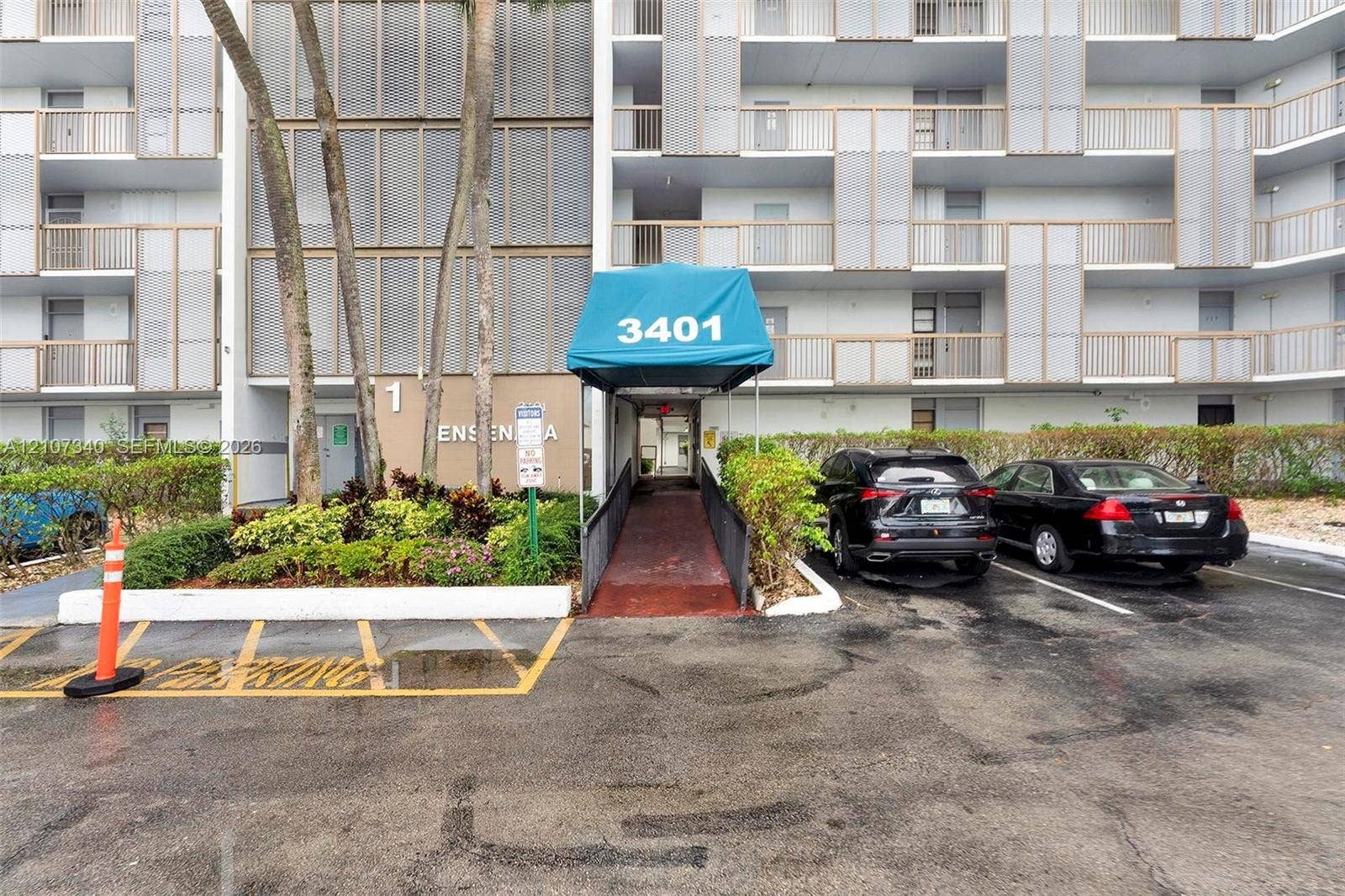 3401 N Country Club Drive, #406, Aventura, Aventura, FL 33180 Multi-story residential building exterior featuring a covered entryway, paved surface parking, and curated landscaping