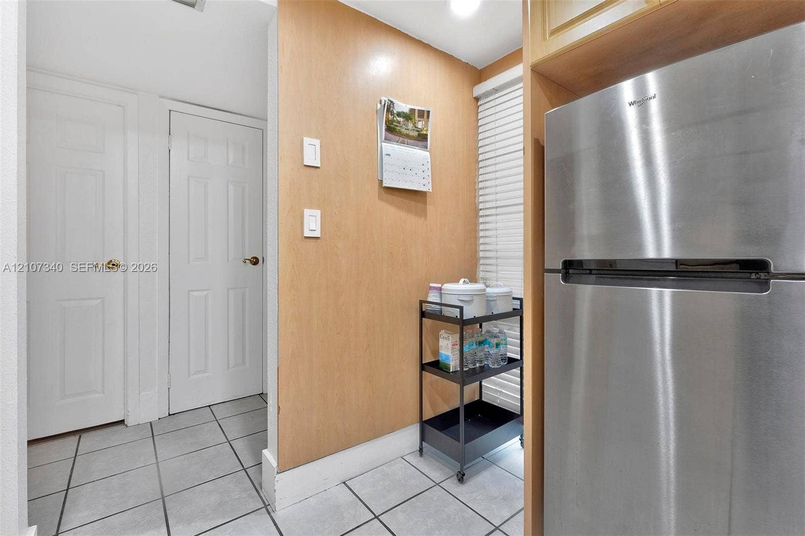 3401 N Country Club Drive, #406, Aventura, Aventura, FL 33180 Stainless steel refrigerator, light-toned wood-finish wall paneling, white six-panel doors with metallic hardware, and ceramic tile flooring