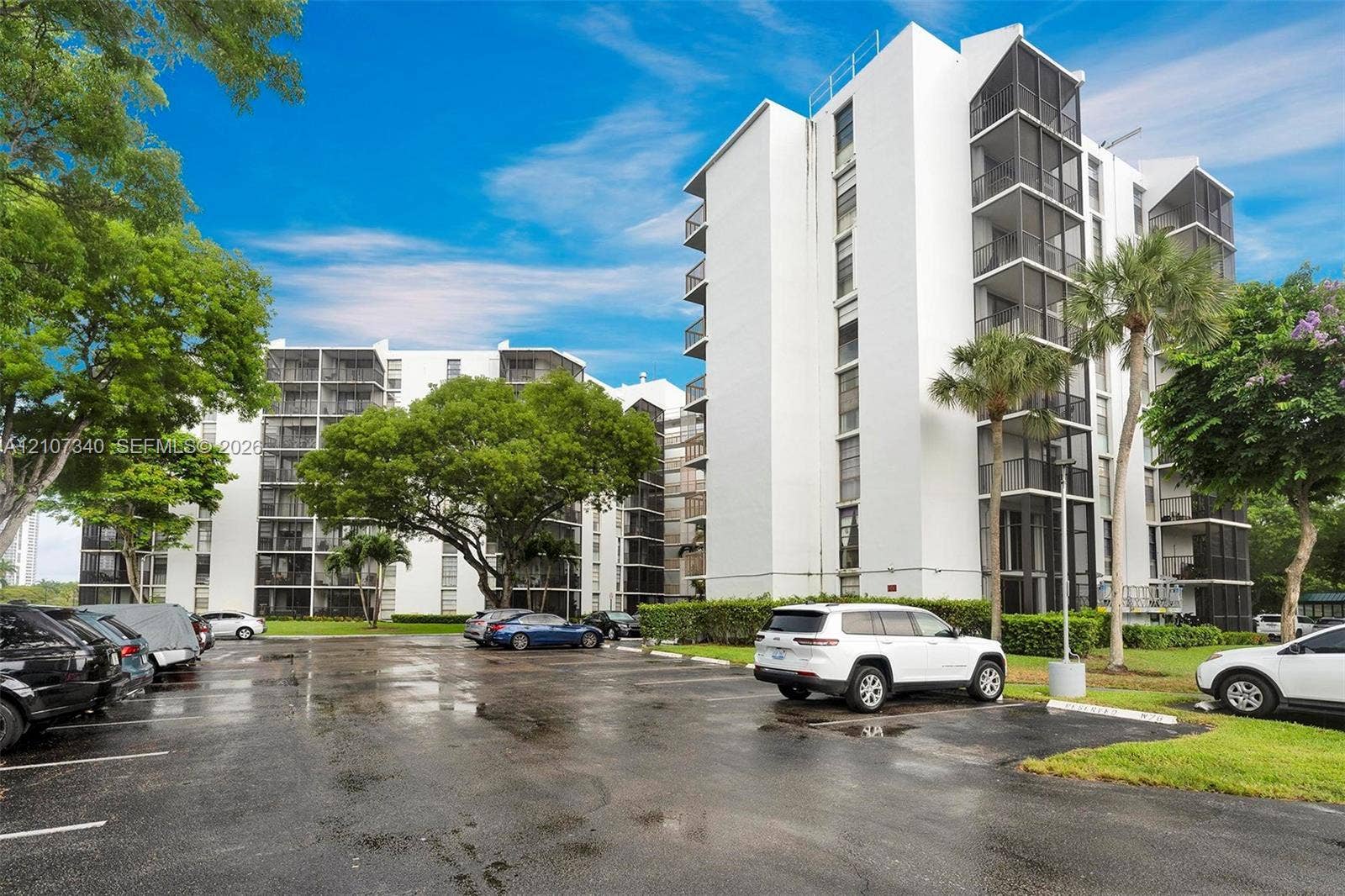 3401 N Country Club Drive, #406, Aventura, Aventura, FL 33180 High-rise residential exterior featuring white stucco siding, screened balconies, and paved surface parking