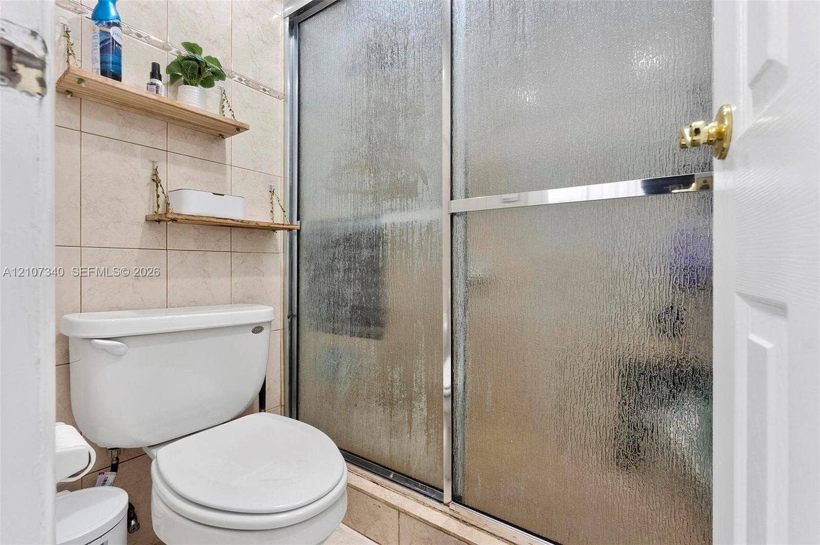 3401 N Country Club Drive, #406, Aventura, Aventura, FL 33180 Bathroom featuring floor-to-ceiling neutral ceramic tile, a glass shower enclosure with metal framing, and wall-mounted shelving