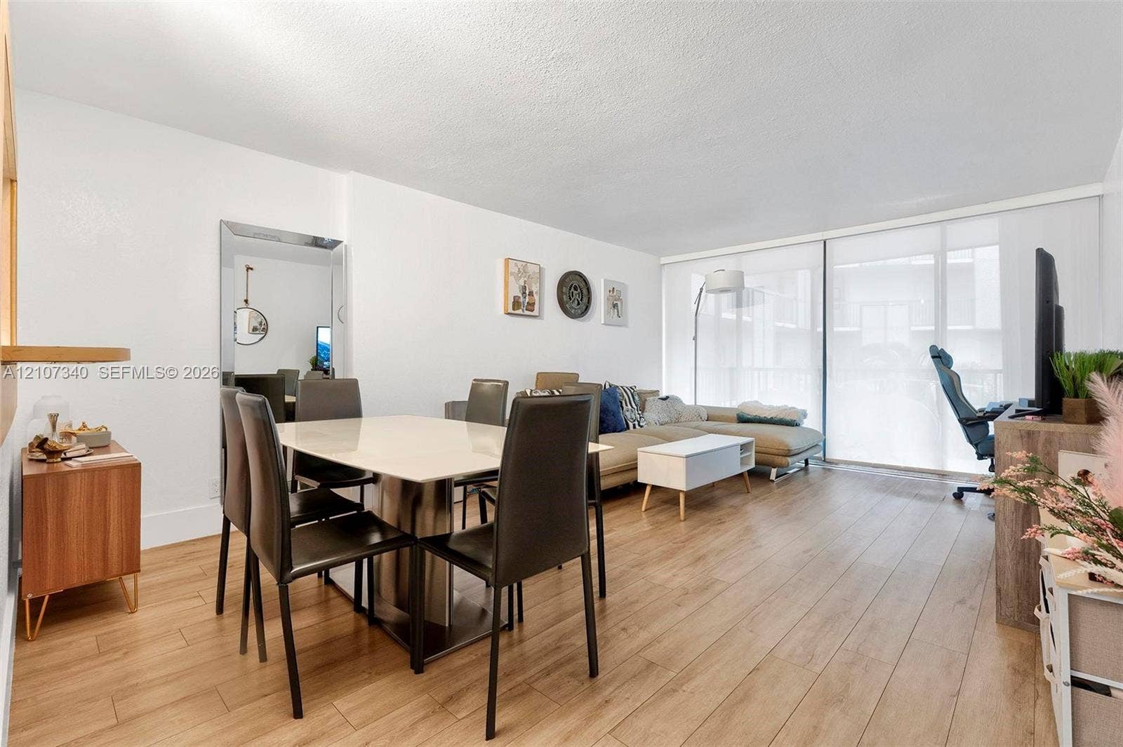 3401 N Country Club Drive, #406, Aventura, Aventura, FL 33180 Open-concept living space featuring wood-finish flooring, a full-length wall mirror, and floor-to-ceiling sliding glass doors with roller shades