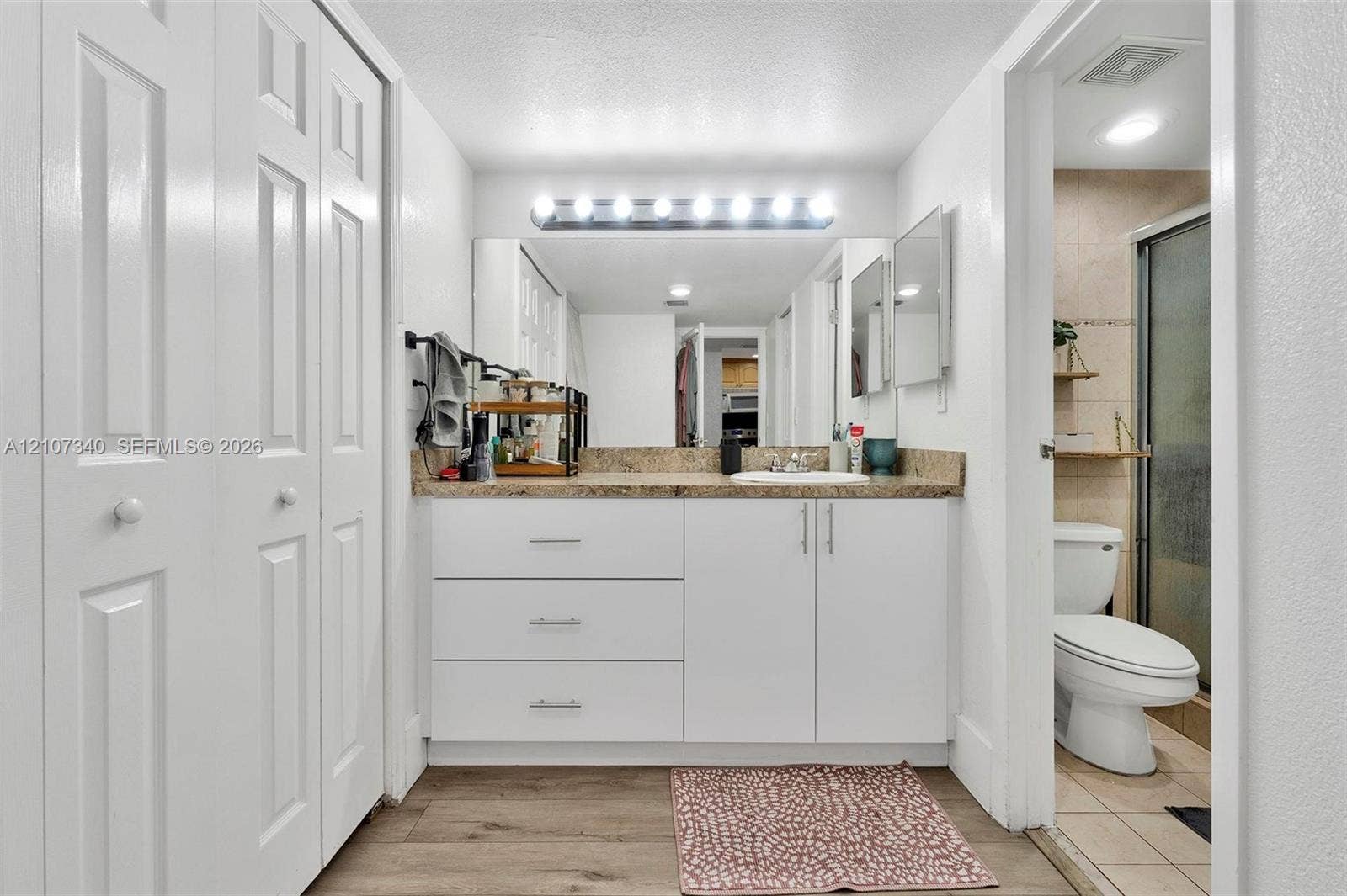 3401 N Country Club Drive, #406, Aventura, Aventura, FL 33180 Bathroom featuring white cabinetry, stone-finish countertop with an integrated basin, full-width wall mirror, multi-bulb vanity lighting, and wood-finish flooring