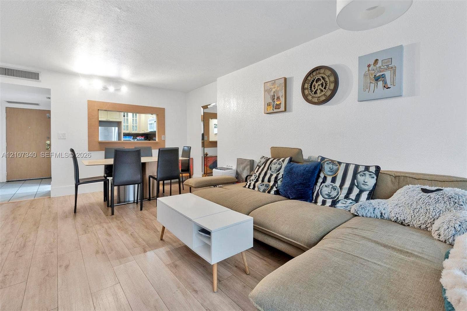 3401 N Country Club Drive, #406, Aventura, Aventura, FL 33180 Open-concept interior featuring light-tone wood-finish flooring, a pass-through window with wood trim, neutral wall finishes, and a contemporary ceiling-mounted light fixture