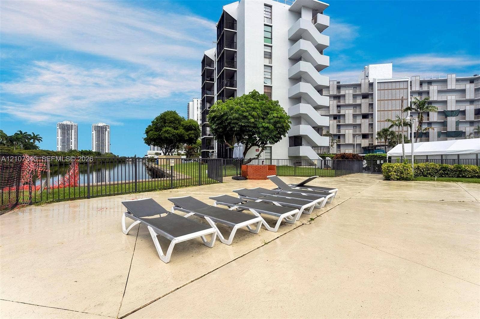 3401 N Country Club Drive, #406, Aventura, Aventura, FL 33180 Concrete pool deck featuring a metal perimeter fence, water frontage, and mature landscaping