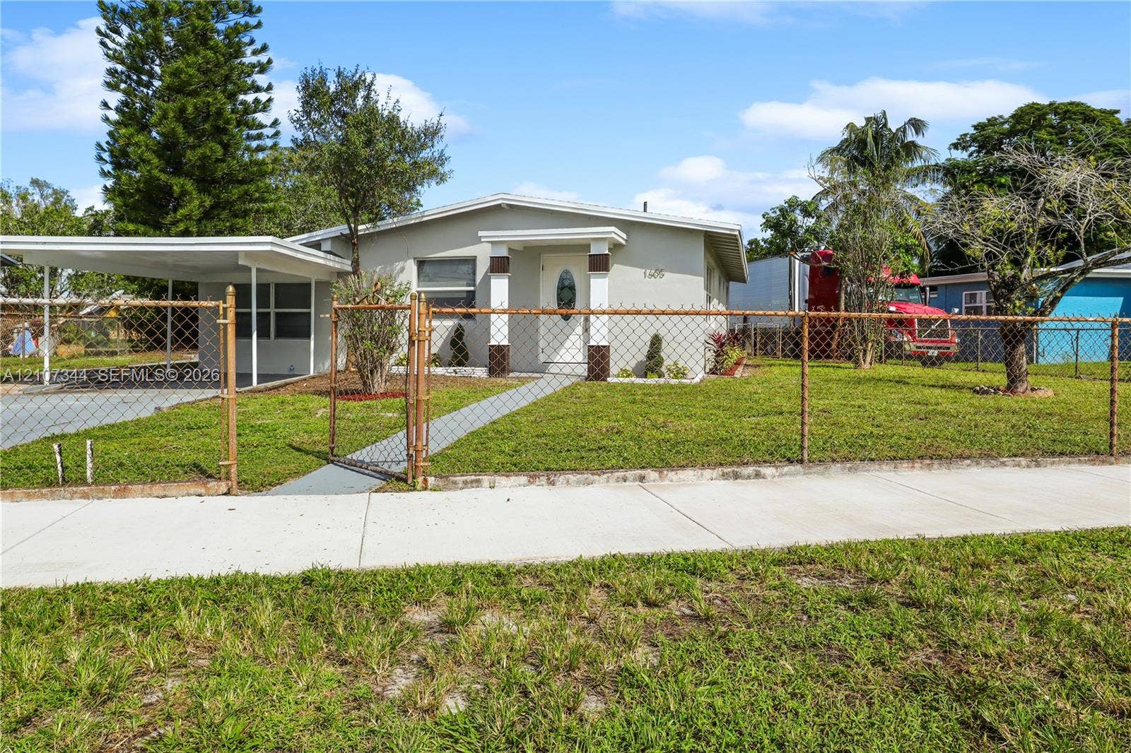 Single-story exterior featuring a covered carport, concrete walkway, and fenced yard