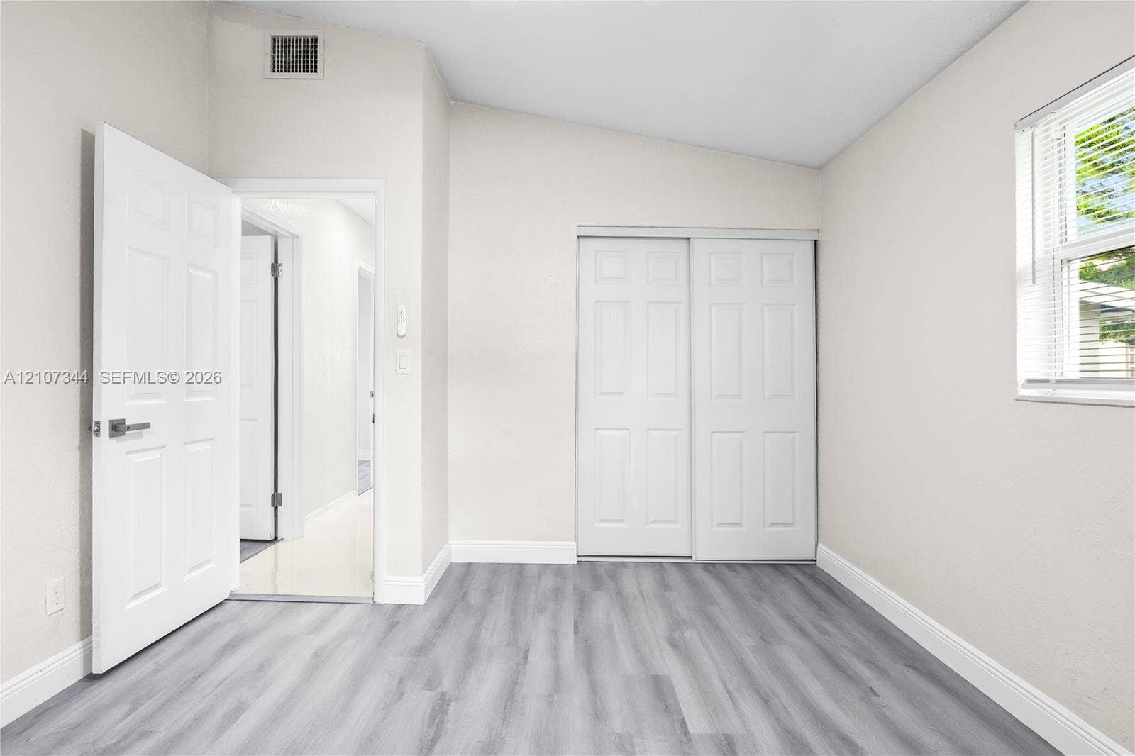 Room featuring wood-finish flooring, a vaulted ceiling, sliding-panel closet doors, and a single-hung window with horizontal blinds