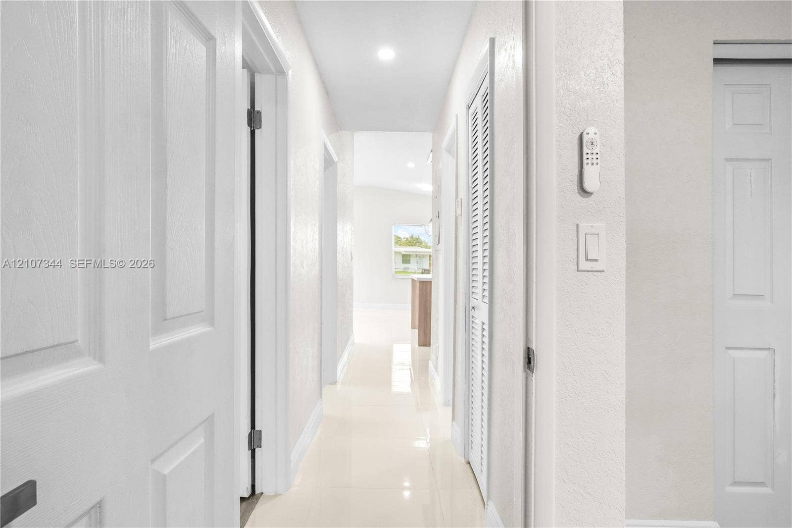 Hallway featuring light-toned tile flooring, recessed ceiling lighting, and crisp white interior doors with louvered closet paneling