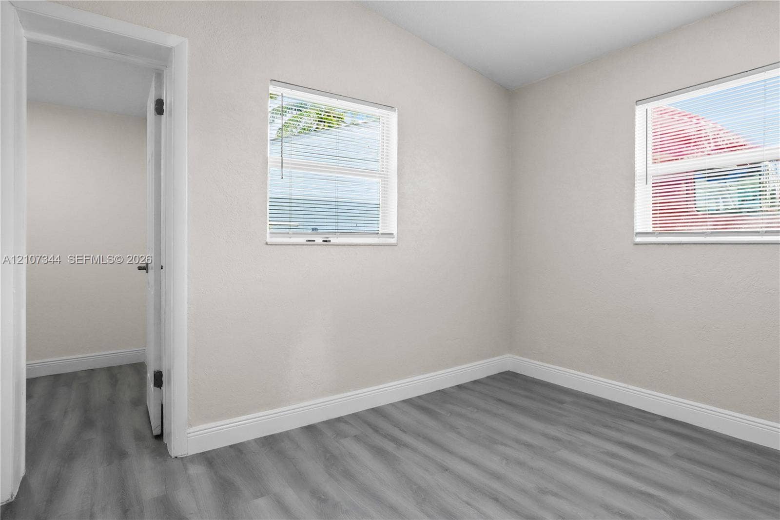 Interior room featuring neutral-toned walls, wood-finish flooring, and two windows with horizontal blinds