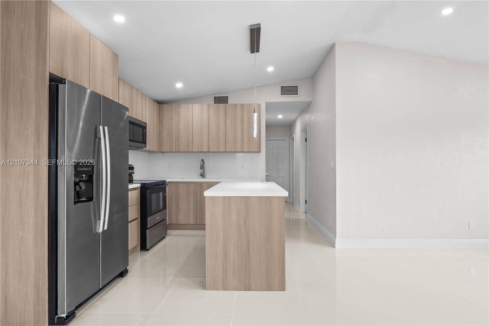 Kitchen featuring light wood-finish cabinetry, a central island with a white countertop, stainless steel appliances, and large-format tile flooring