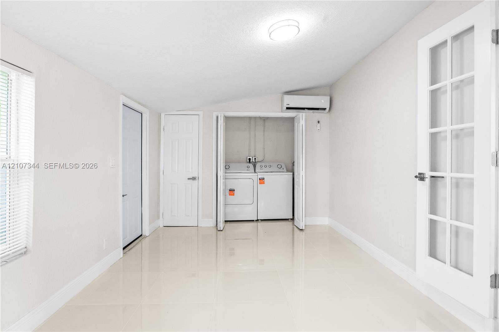 Large-format tile flooring, wall-mounted ductless air conditioning unit, French door with glass panes, and enclosed laundry closet