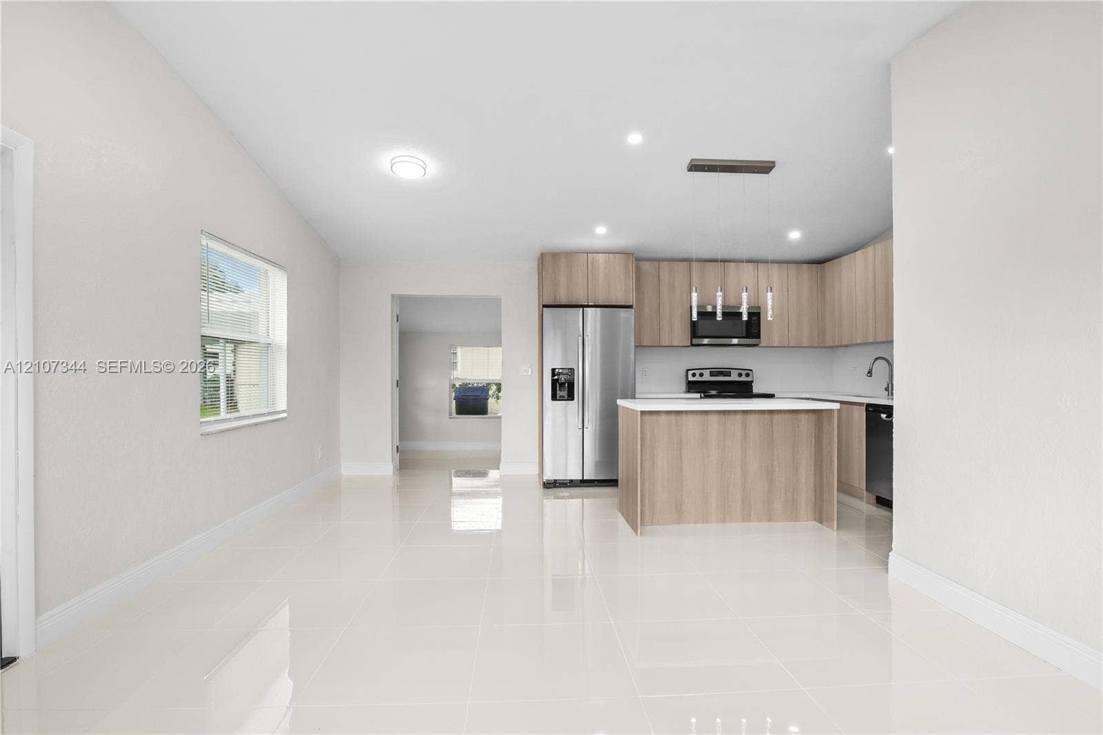 Kitchen featuring wood-finish cabinetry, stainless steel appliances, a central island with white countertop, and polished tile flooring