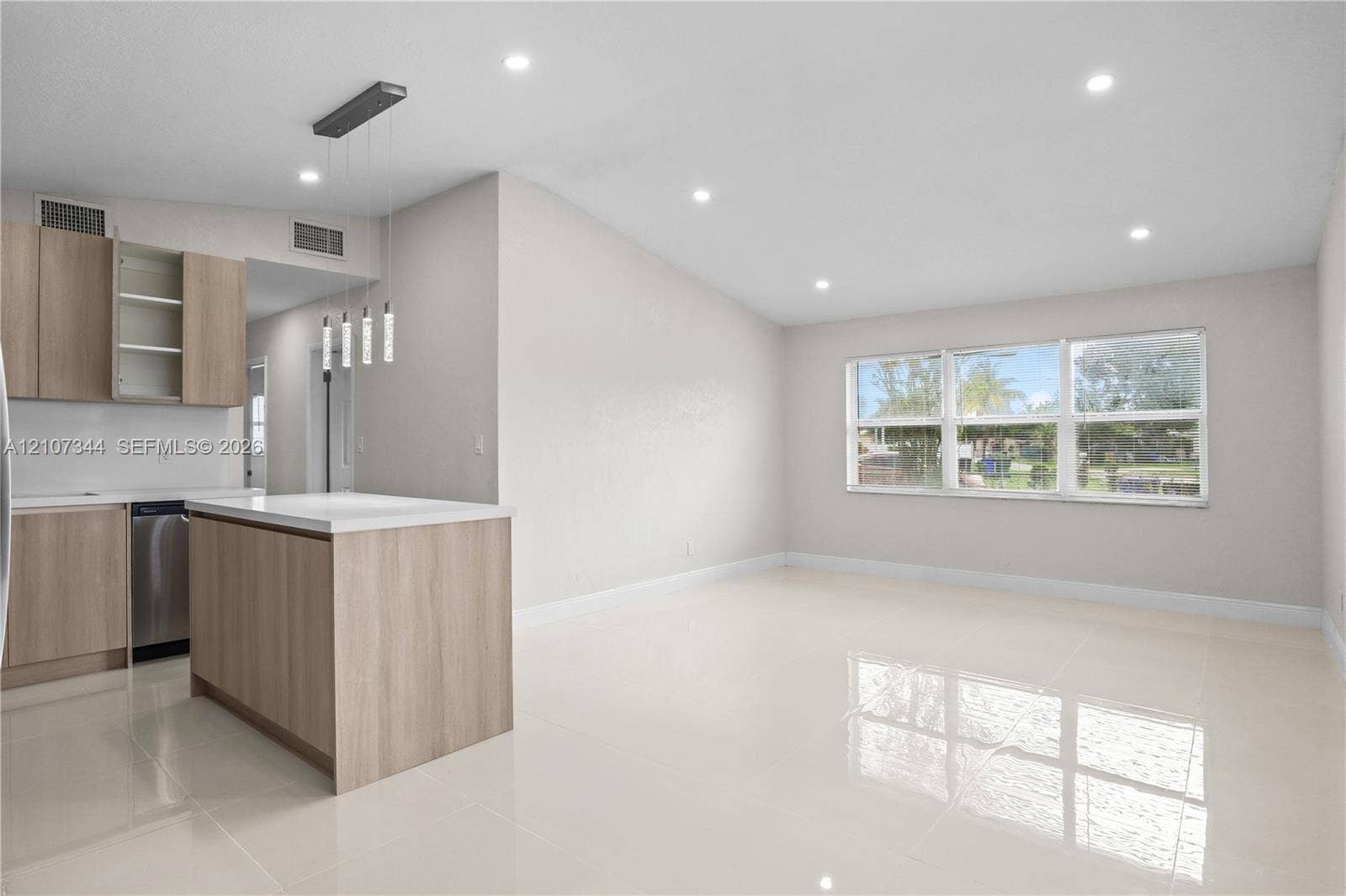Kitchen featuring light wood-finish cabinetry, a central island with a white countertop, polished tile flooring, recessed ceiling lighting, and large windows