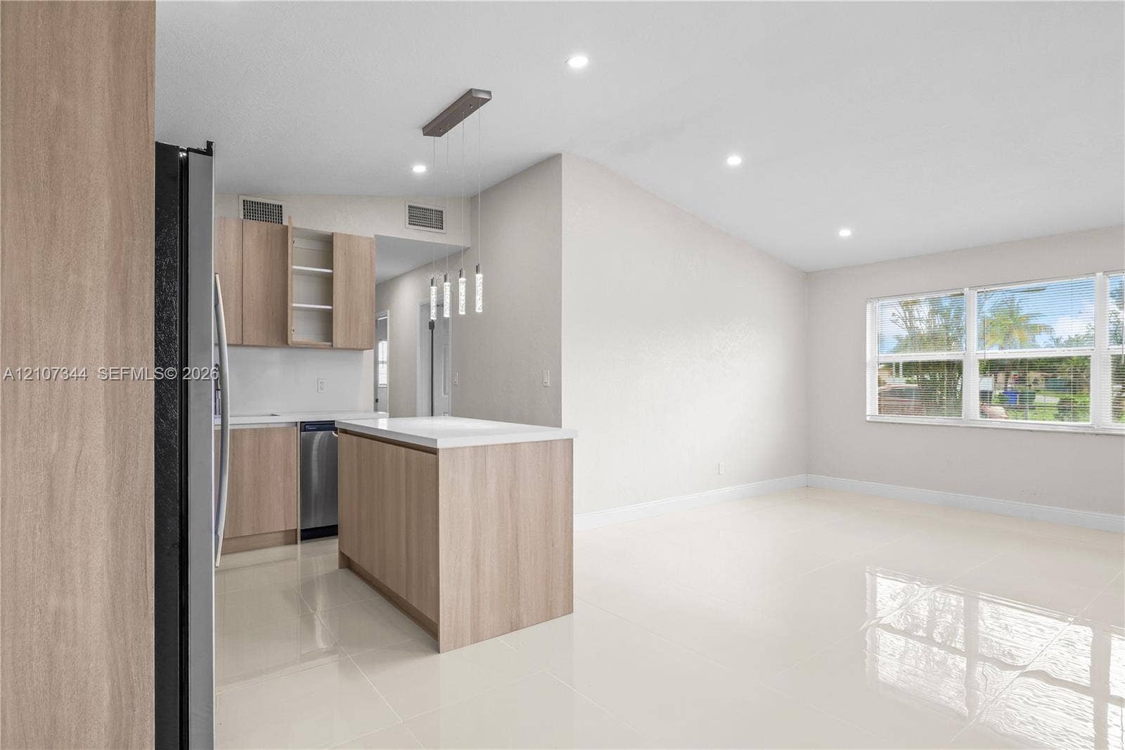 Open-concept kitchen featuring light wood-finish cabinetry, a central island with a white countertop, recessed lighting, and polished tile flooring