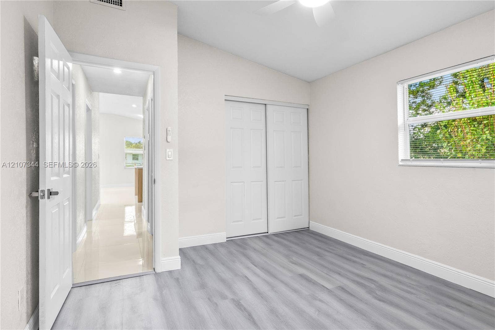 Interior room featuring wood-finish flooring, a ceiling fan, a window with horizontal blinds, and a closet with double sliding doors