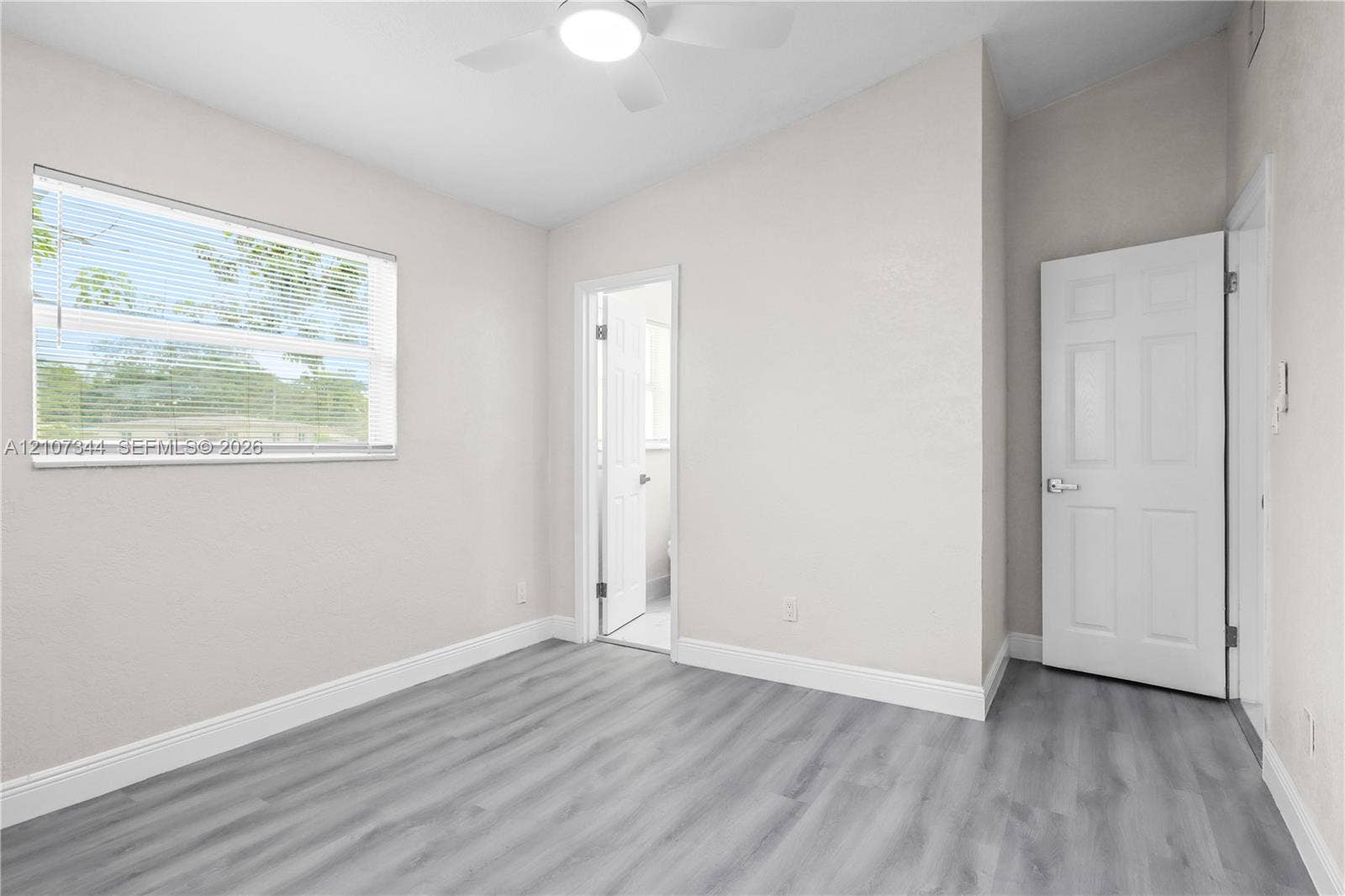 Room featuring wood-finish flooring, vaulted ceilings, a ceiling fan with integrated lighting, and a six-panel interior door