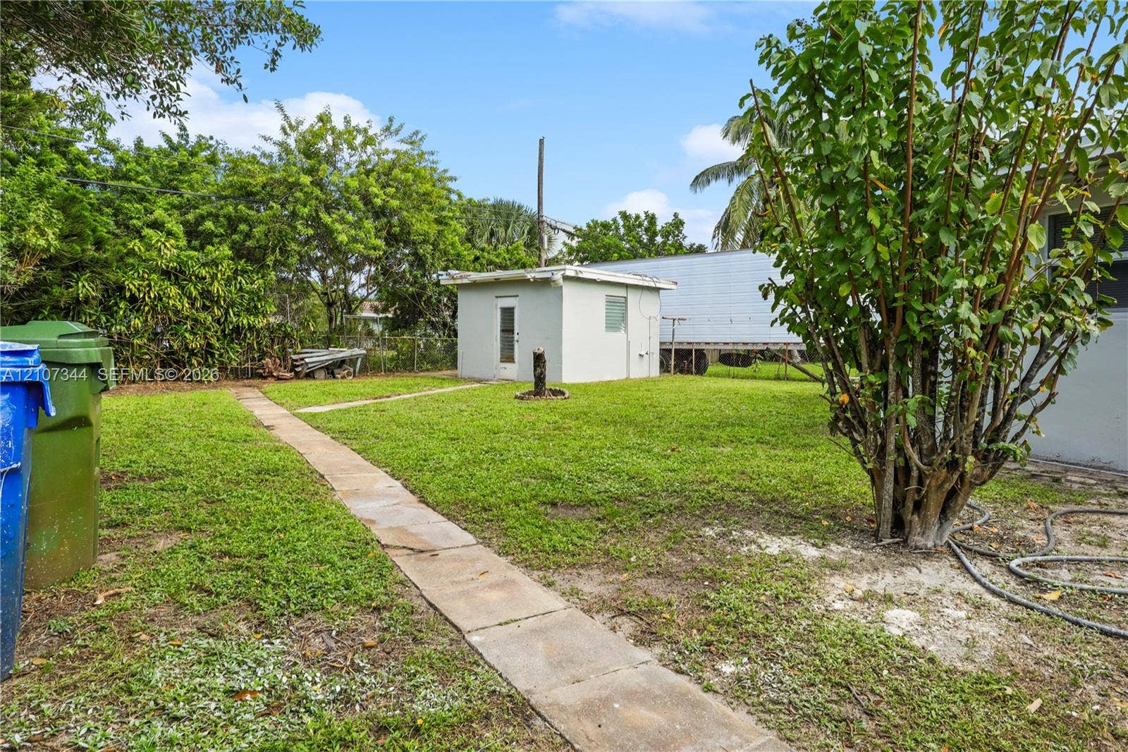 Exterior area featuring a grass lawn, a detached structure with a single entry door, and a concrete walkway