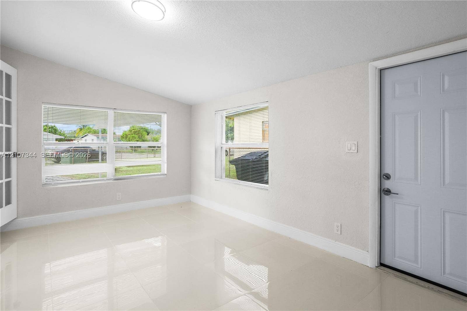 Neutral-toned interior featuring large-format tile flooring, multiple windows, a multi-panel entry door, and a multi-lite French door