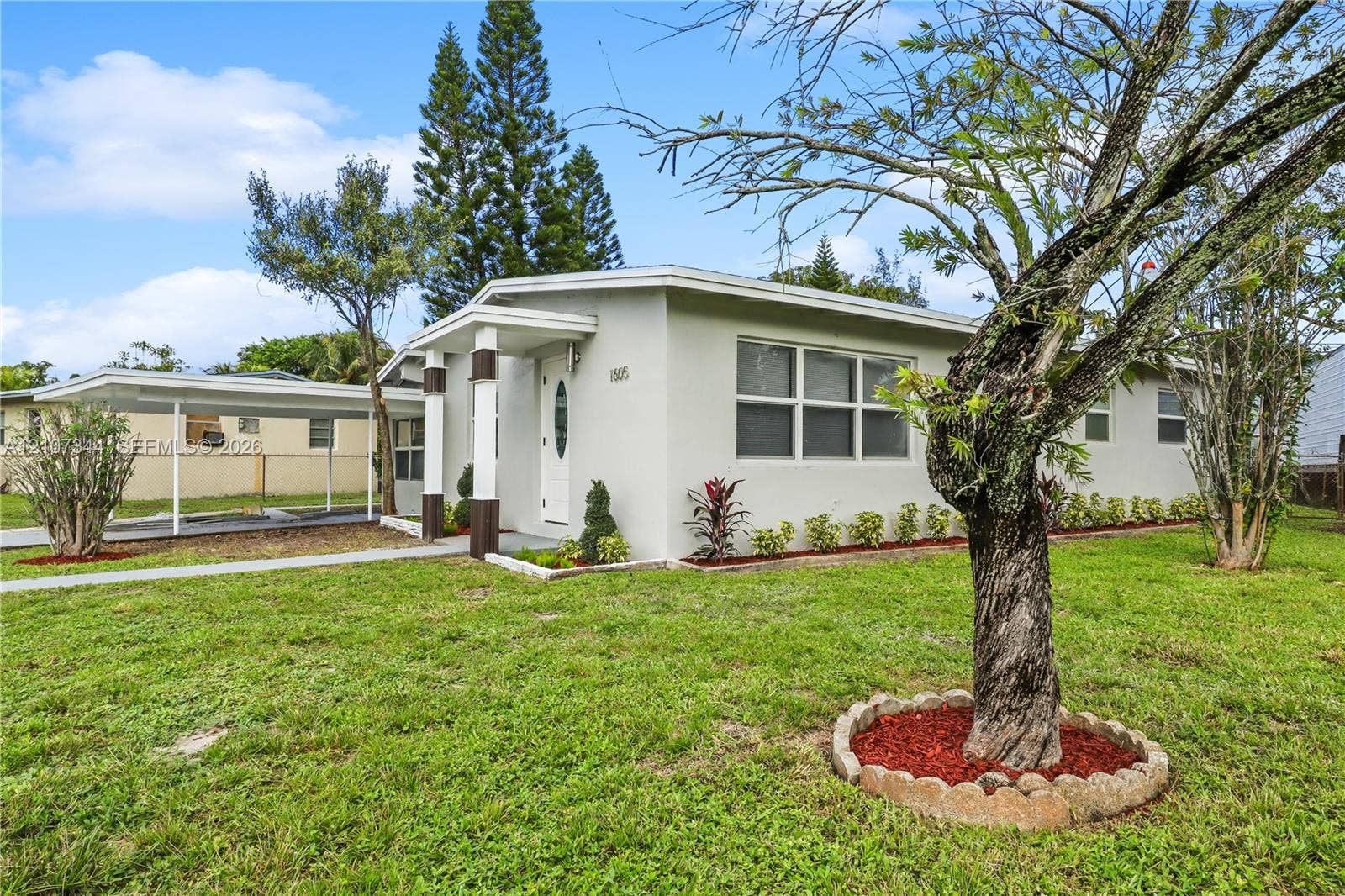 Stucco exterior residence featuring a covered carport, concrete walkway, and landscaped garden beds with stone edging