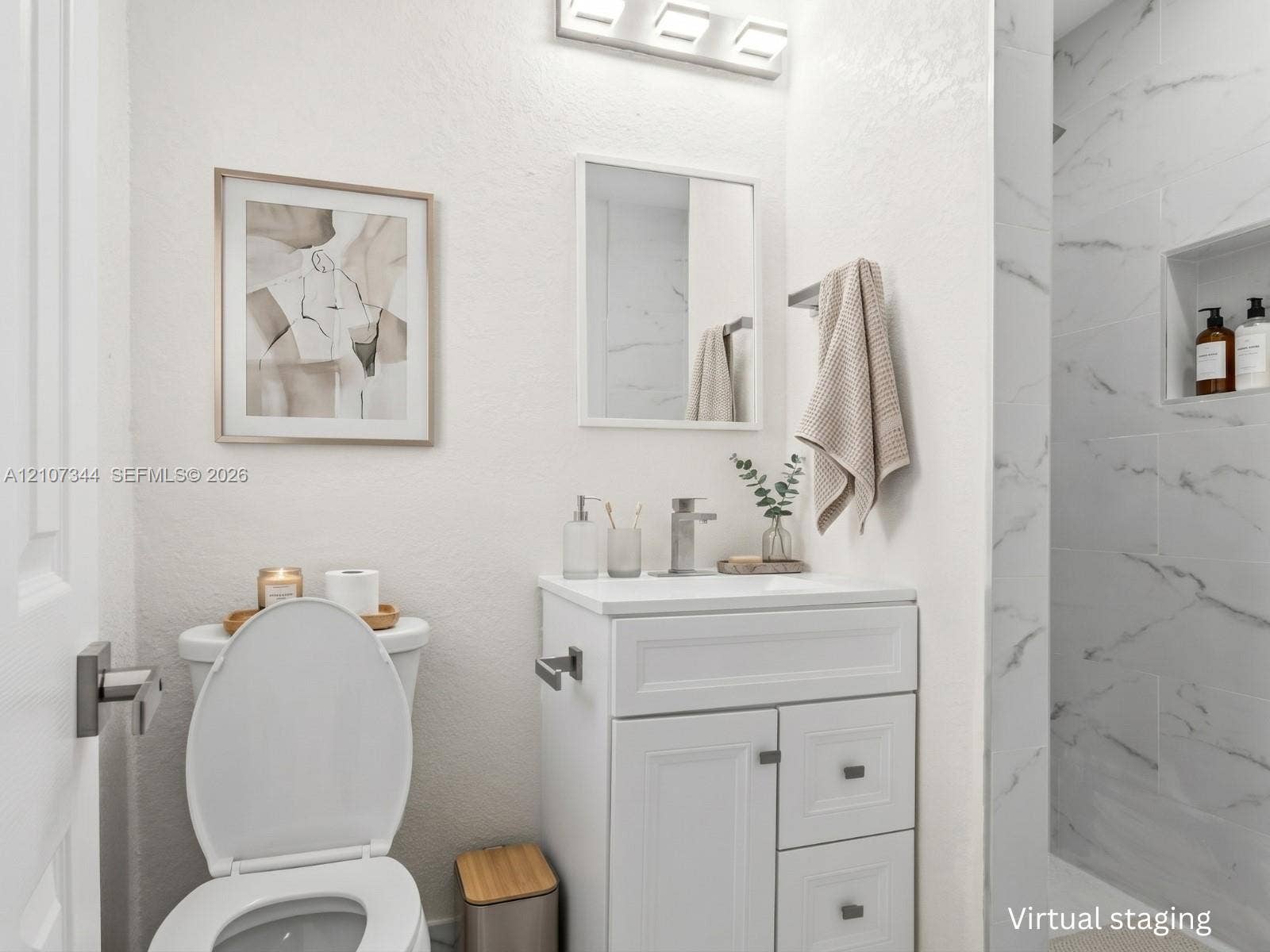 Bathroom vanity with white cabinetry and a rectangular sink, brushed nickel faucet, wall-mounted light fixture, and shower surround with stone-finish tile and a built-in recessed niche