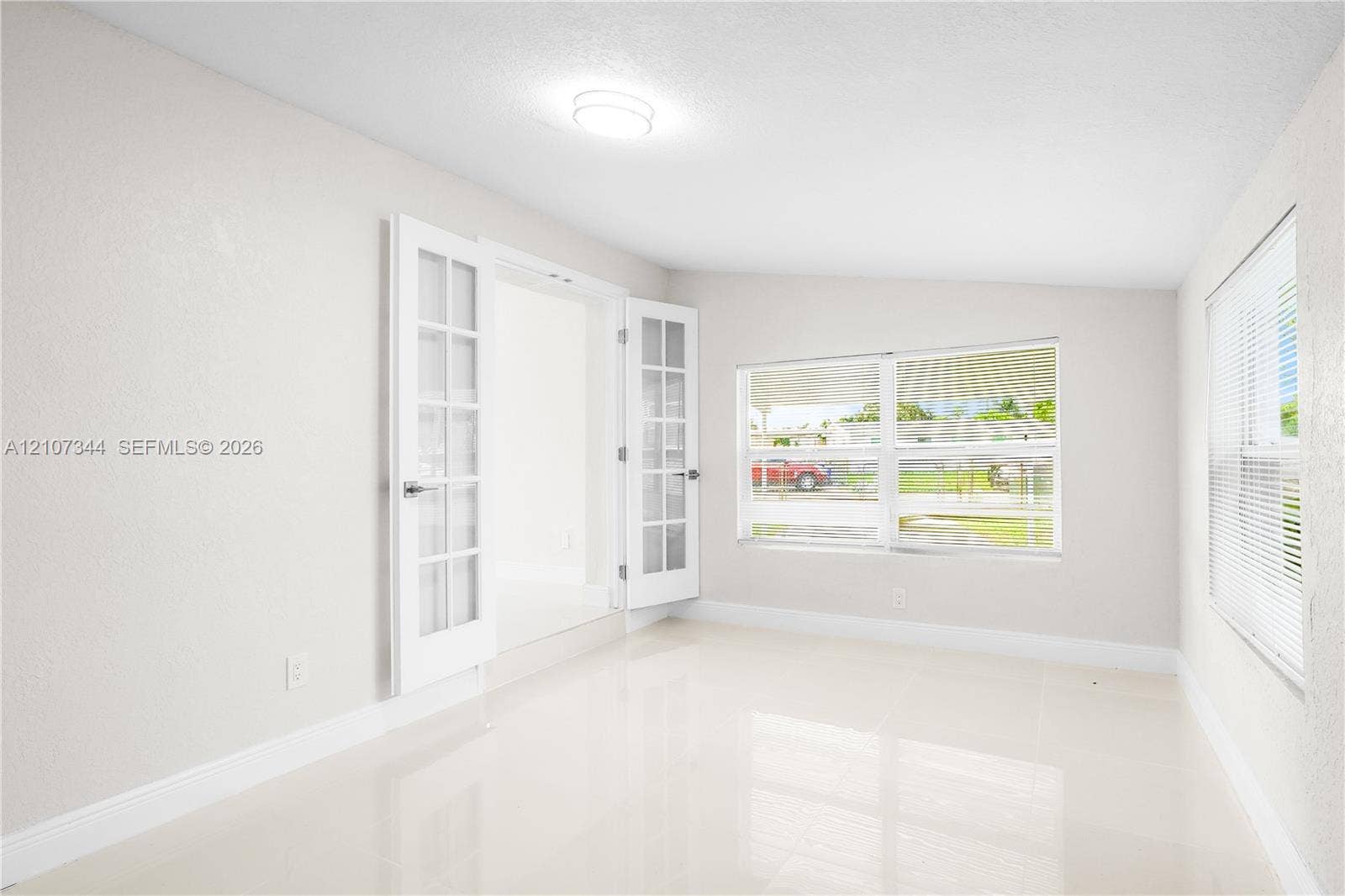Bright interior featuring polished tile flooring, white French doors with glass panes, flush-mount ceiling lighting, and large windows with horizontal blinds