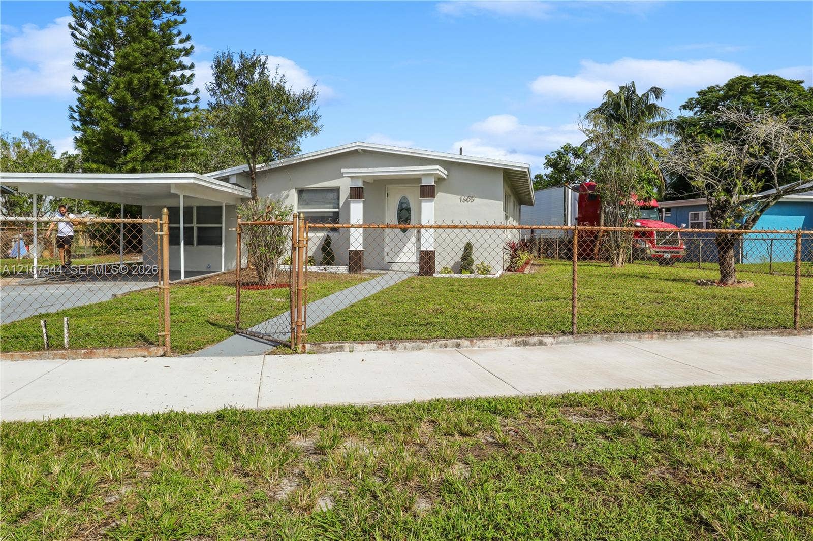 Single-story residence featuring a covered carport, concrete walkway, and chain-link perimeter fencing