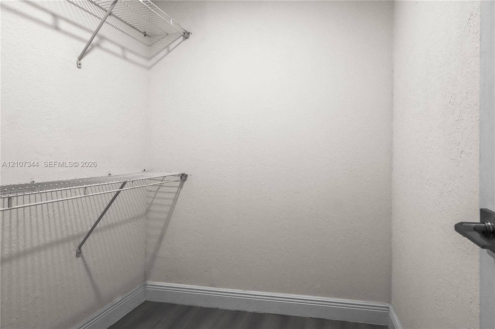 Storage space featuring dual-tier white wire shelving and grey wood-finish flooring