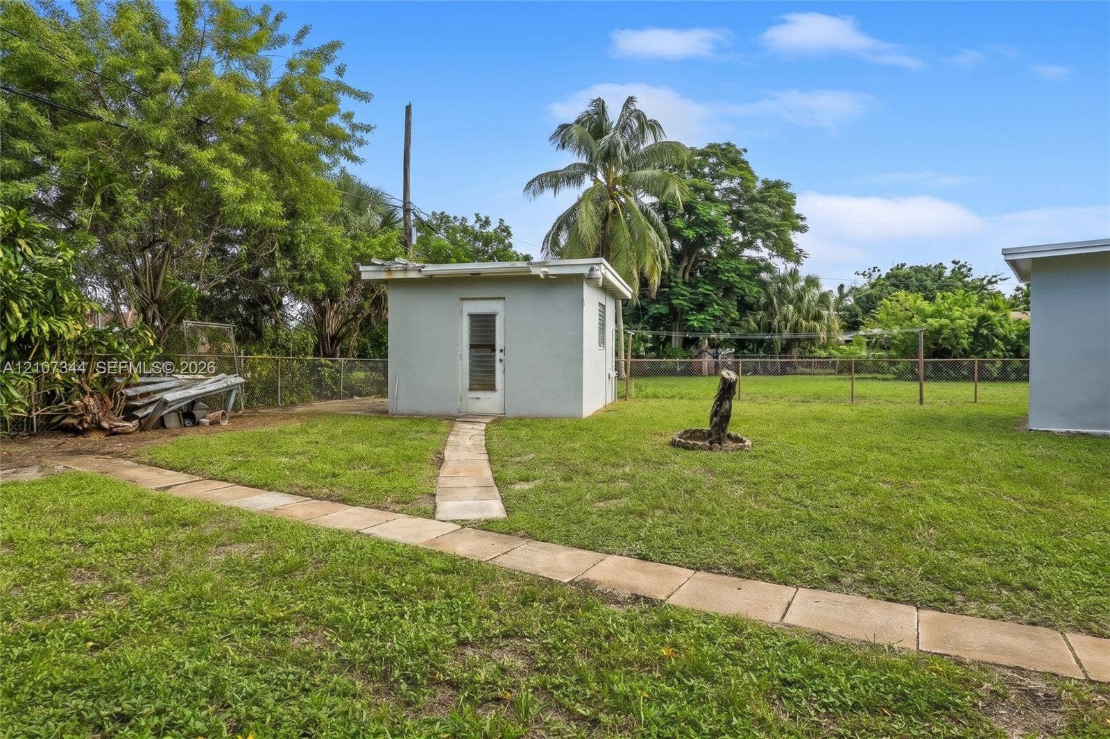 Backyard featuring a grass lawn, paved walkways, detached exterior structure, and perimeter fencing