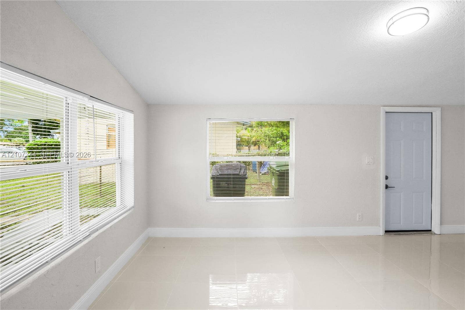 Bright interior space featuring polished tile flooring, neutral wall tones, large double-pane windows, and a flush-mount overhead light fixture