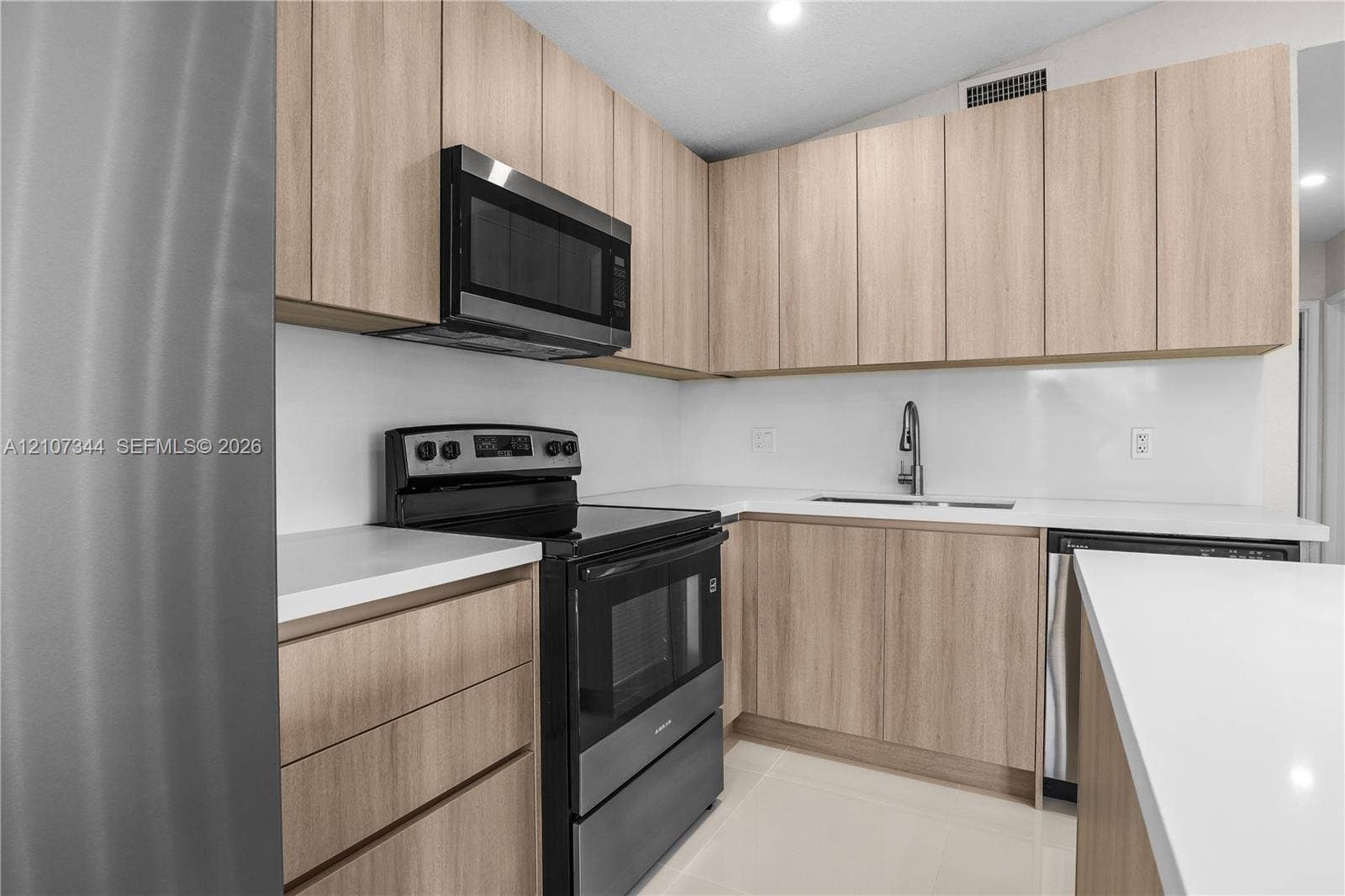 Kitchen featuring light wood-finish cabinetry, solid surface countertops, stainless steel appliances, and a modern gooseneck faucet