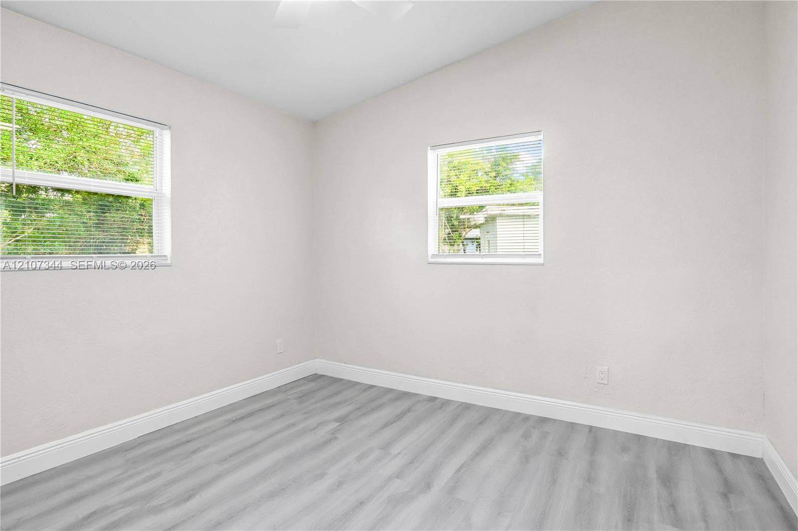 Neutral-toned interior space featuring vaulted ceilings, wood-finish flooring, and two windows with horizontal blinds
