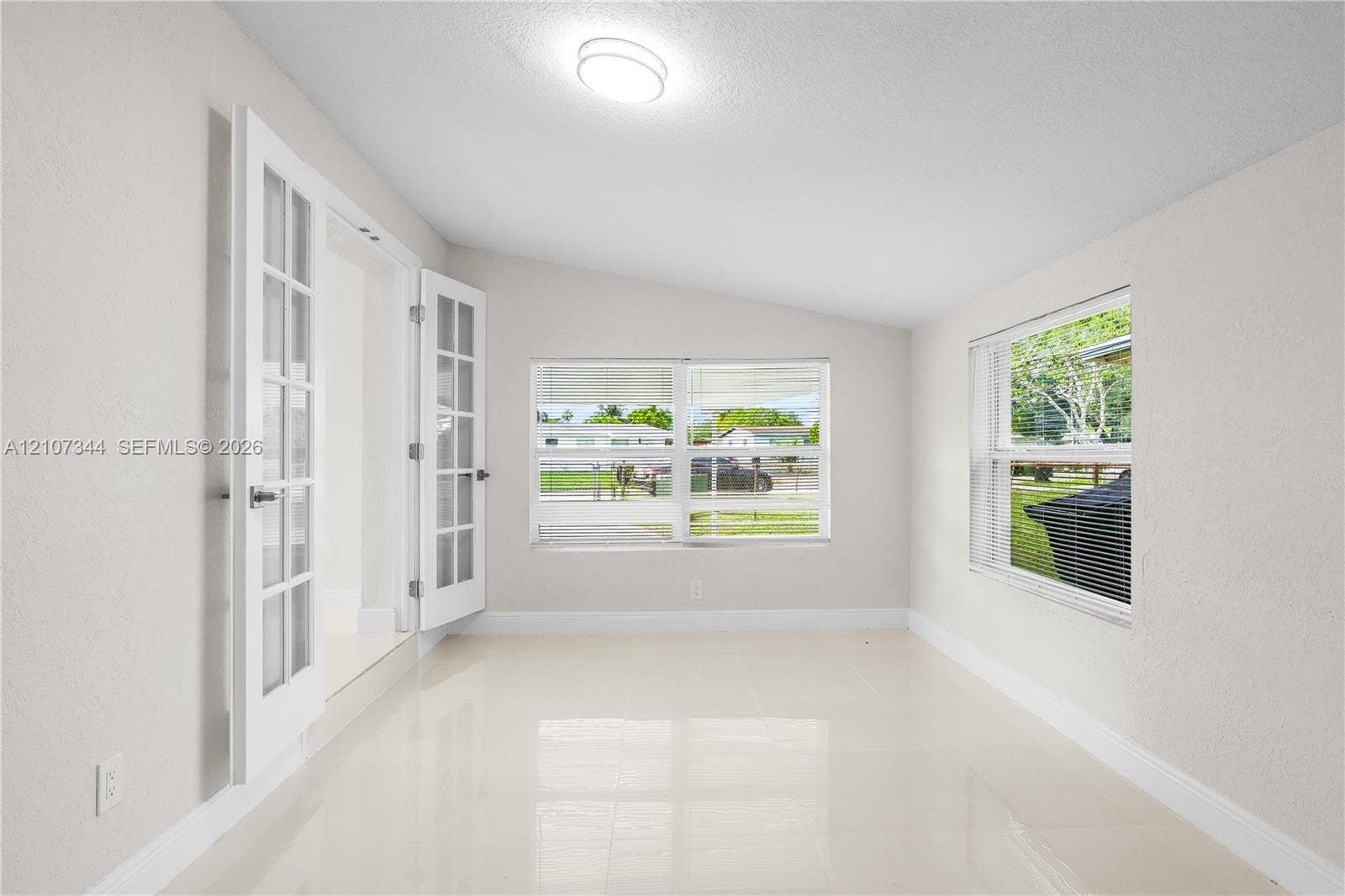 Bright sunroom featuring light-toned tile flooring, white-painted walls, dual French doors with glass panes, and large picture windows