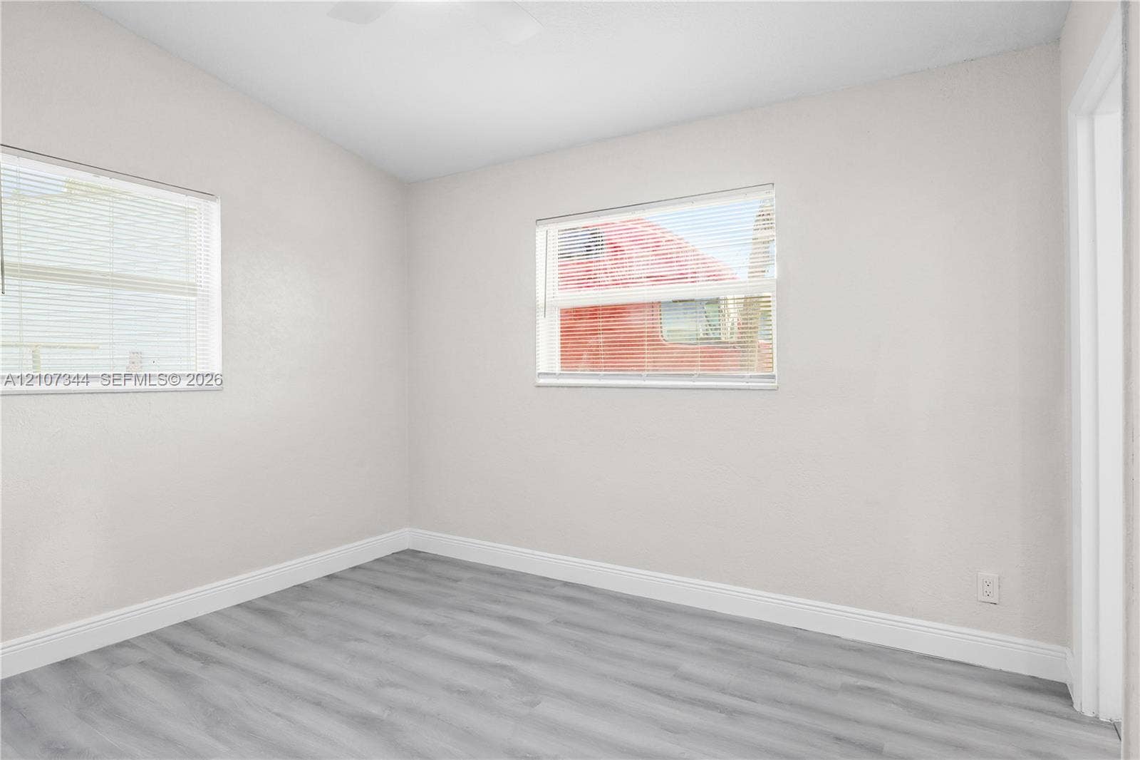 Room featuring neutral wall paint, wood-finish flooring, and dual windows with horizontal blinds