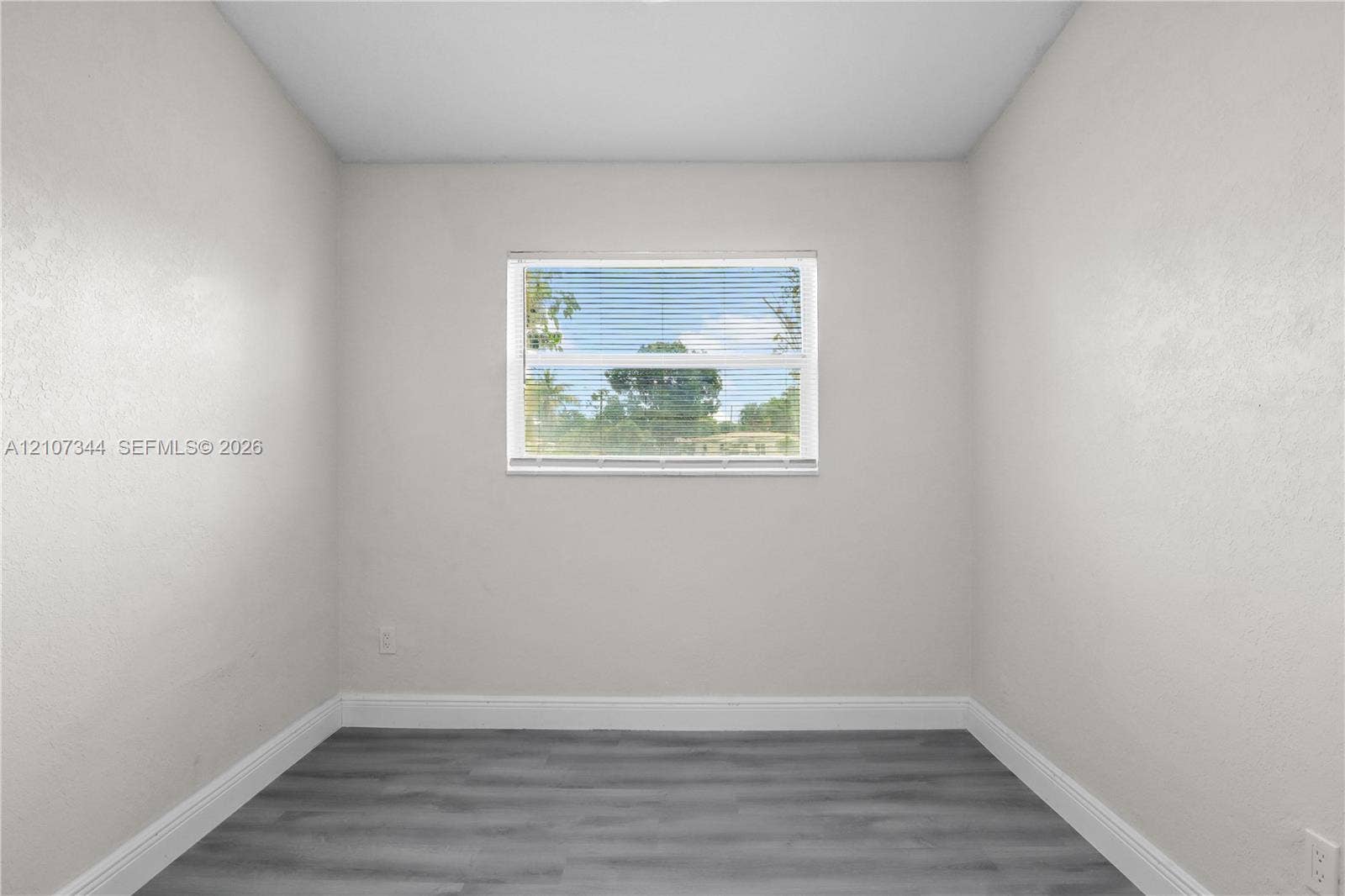 Interior space featuring neutral-toned walls, wood-finish flooring, and a central window with horizontal blinds