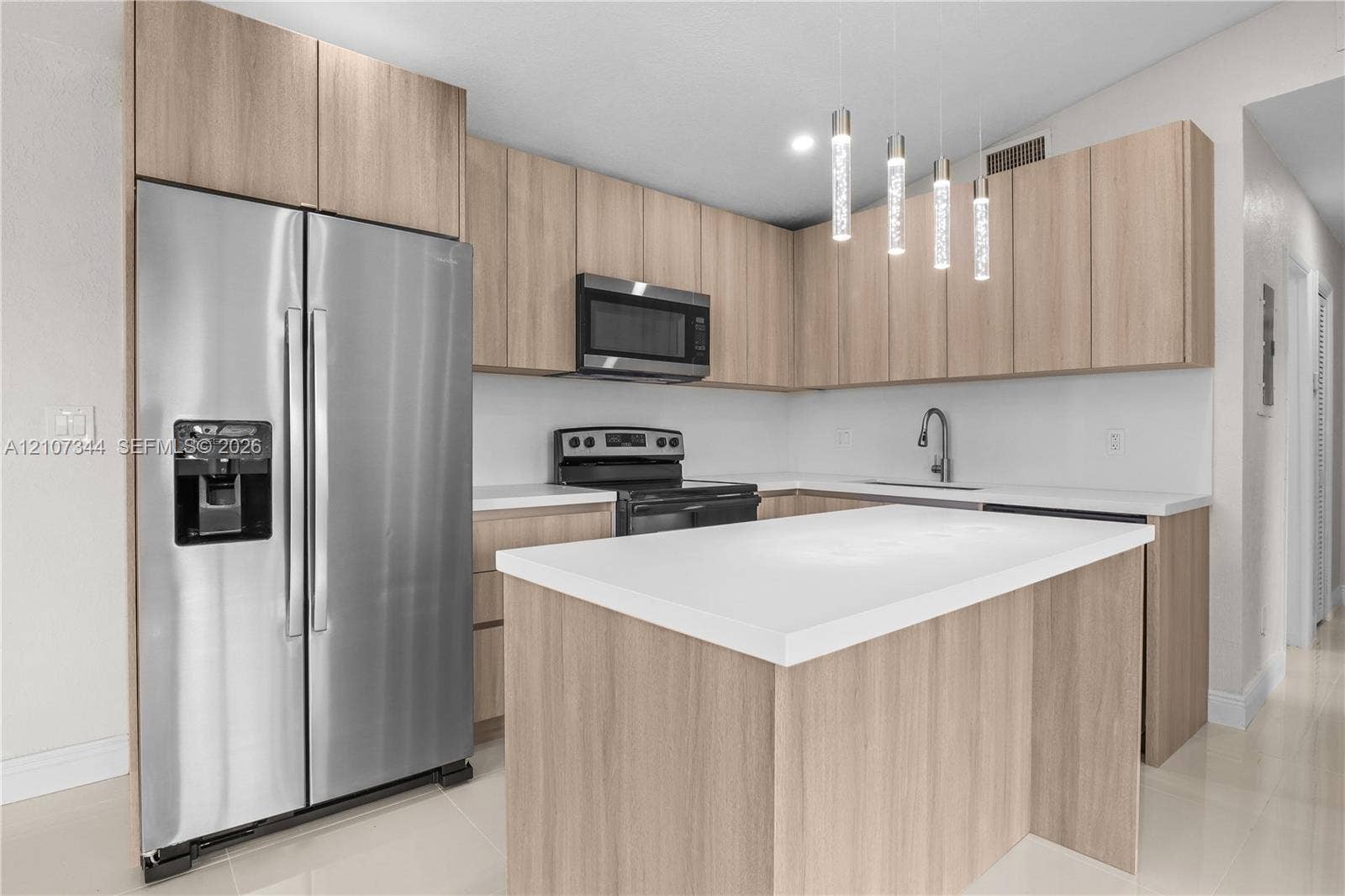 Kitchen featuring light wood-finish cabinetry, quartz countertops, stainless steel appliances, and four modern cylindrical pendant lights