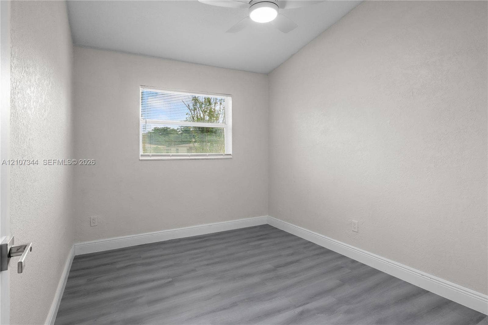 Neutral-toned interior space featuring wood-finish flooring, a ceiling fan with integrated lighting, and a single-pane window