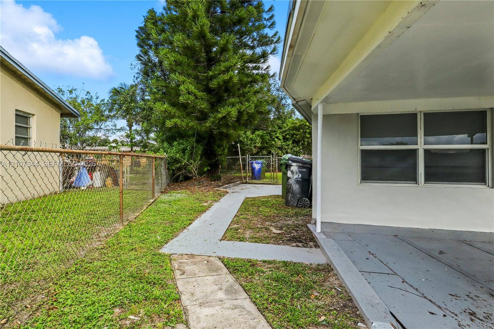 Covered rear patio featuring a concrete floor, painted masonry exterior walls, and a perimeter chain-link fence