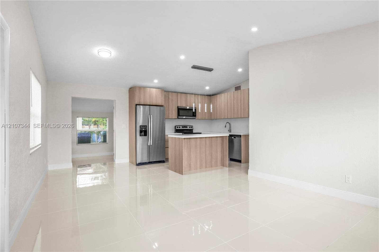 Kitchen featuring light-tone wood cabinetry, a center island with a stone-surface countertop, stainless steel appliances, and large-format porcelain tile flooring