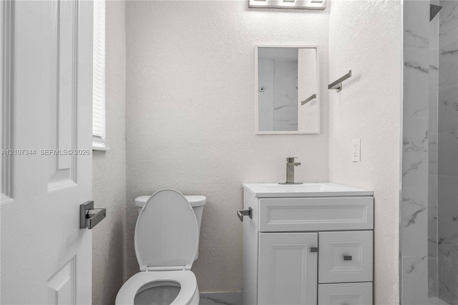White vanity with integrated basin, single-handle faucet, rectangular wall mirror, and walk-in shower featuring tiled surround