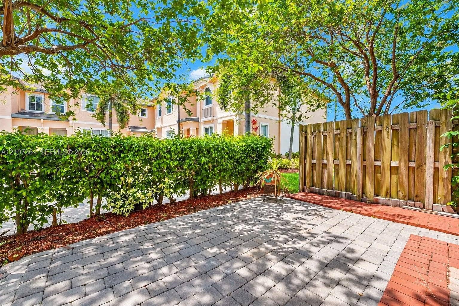 230 SE 29th Avenue, #1, Homestead, Homestead, FL 33033 Exterior patio featuring interlocking concrete pavers, red brick border, privacy wood fencing, and perimeter hedging