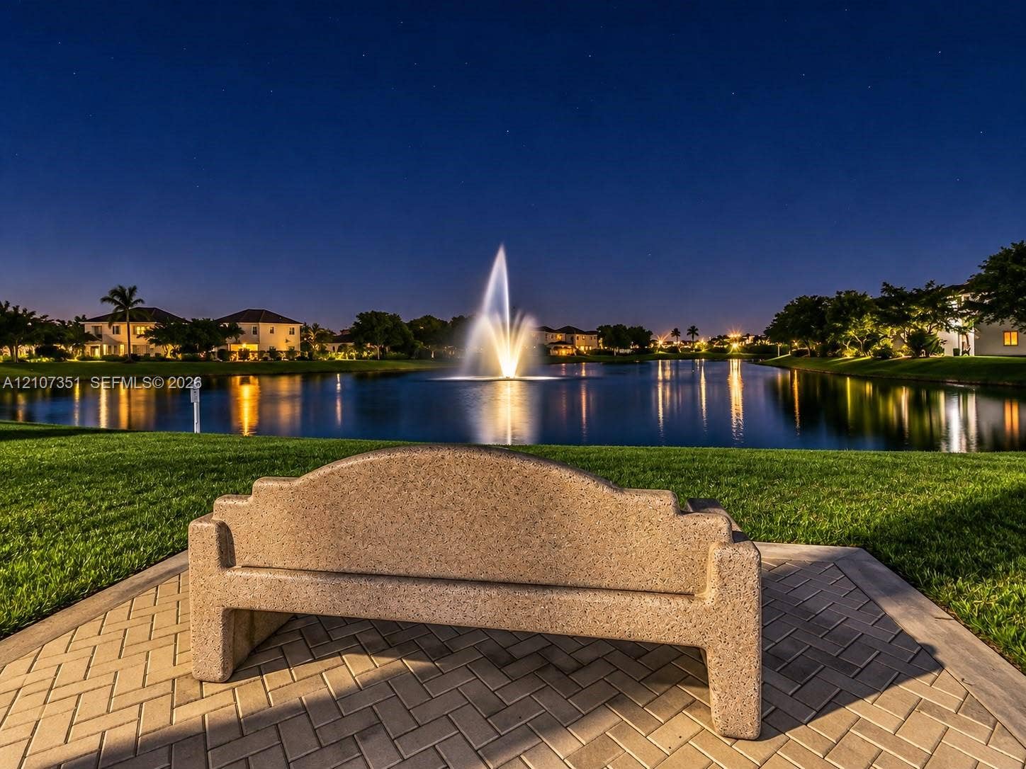 230 SE 29th Avenue, #1, Homestead, Homestead, FL 33033 Concrete bench situated on a herringbone-pattern paver patio, overlooking a lake with a central water fountain and surrounding manicured turf