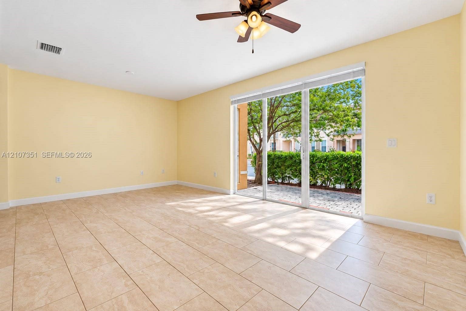230 SE 29th Avenue, #1, Homestead, Homestead, FL 33033 Spacious room featuring neutral tile flooring, a multi-blade ceiling fan with integrated light fixtures, and a glass sliding door opening to a paved patio area