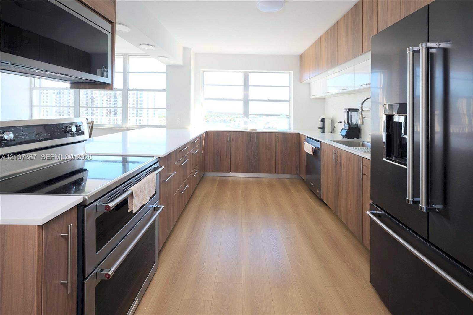 2851 NE 183rd Street, #1617E, Aventura, FL 33160 Galley kitchen featuring wood-finish cabinetry, quartz countertops, stainless steel appliances, and wood-finish flooring