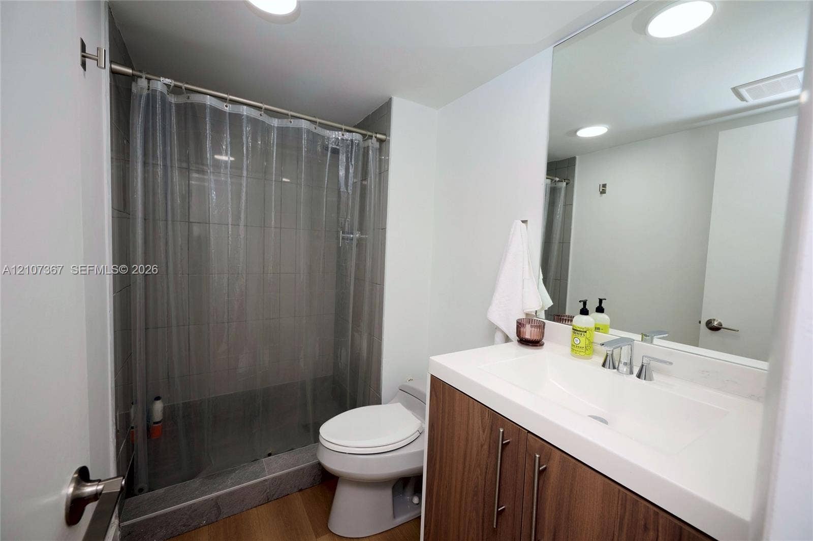 2851 NE 183rd Street, #1617E, Aventura, FL 33160 Bathroom featuring a vanity with a wood-finish cabinet and white integrated countertop, large wall-mounted mirror, recessed ceiling lighting, and a tiled shower surround