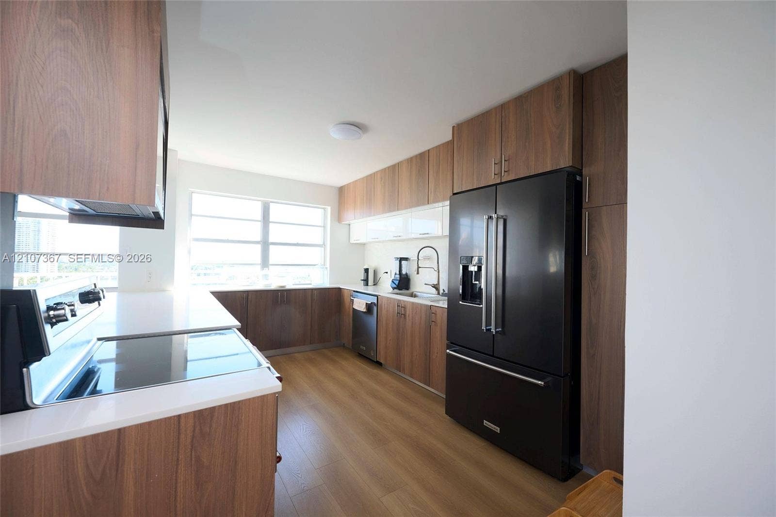 2851 NE 183rd Street, #1617E, Aventura, FL 33160 Kitchen featuring wood-finish cabinetry, solid surface countertops, a stainless-steel sink with a gooseneck faucet, black appliances, and wood-finish flooring