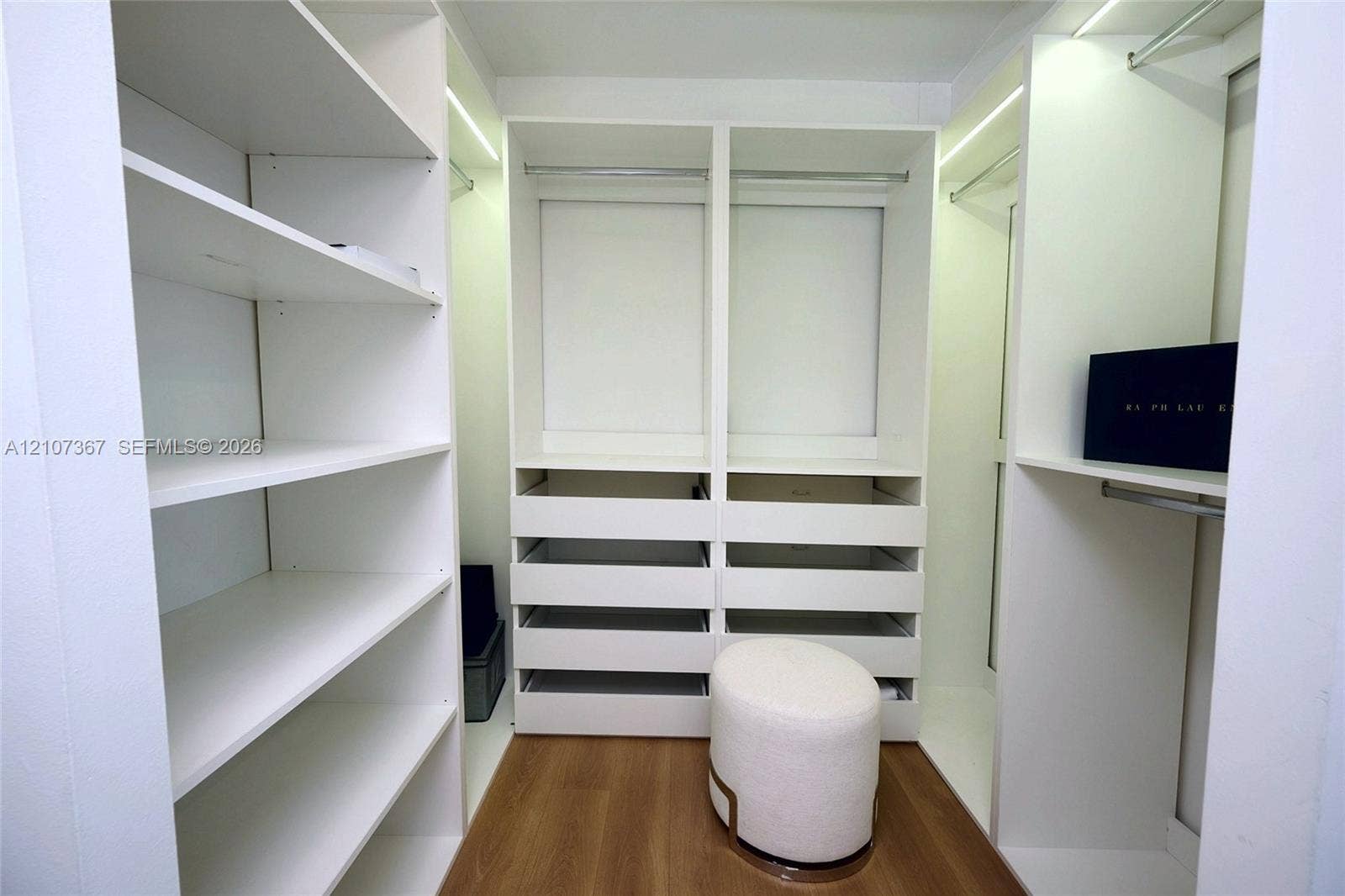 2851 NE 183rd Street, #1617E, Aventura, FL 33160 Custom closet featuring built-in white shelving, integrated hanging rods, tiered pull-out drawers, and wood-finish flooring
