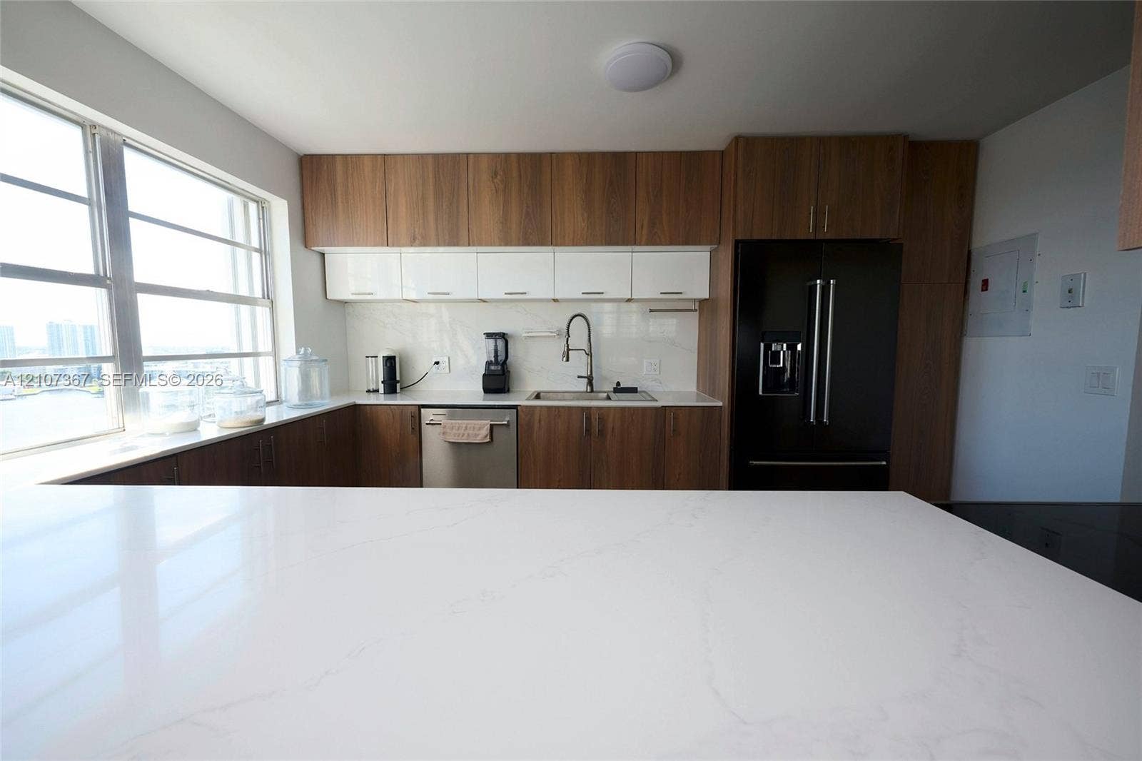 2851 NE 183rd Street, #1617E, Aventura, FL 33160 Kitchen featuring white solid-surface countertops, two-tone wood-finish and high-gloss white cabinetry, stainless steel appliances, and a high-arch pull-down faucet