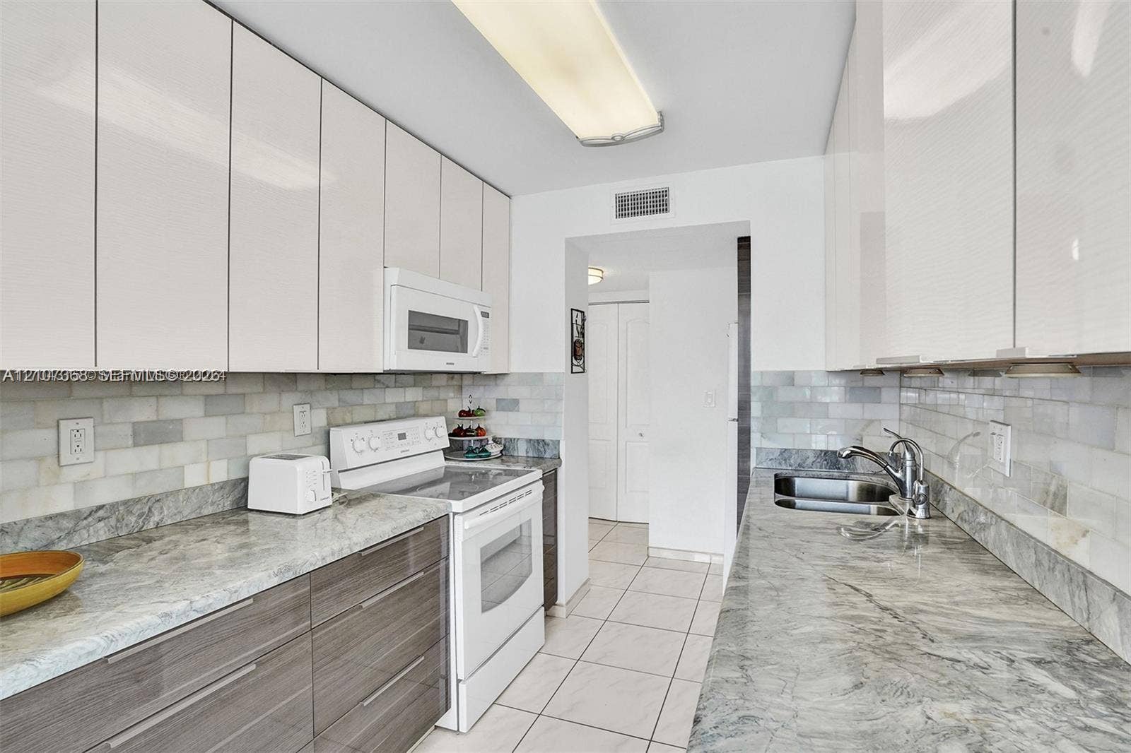 Kitchen featuring high-gloss white upper cabinetry, horizontal grain wood-finish lower cabinets, stone countertops, a subway tile backsplash, and ceramic floor tiling