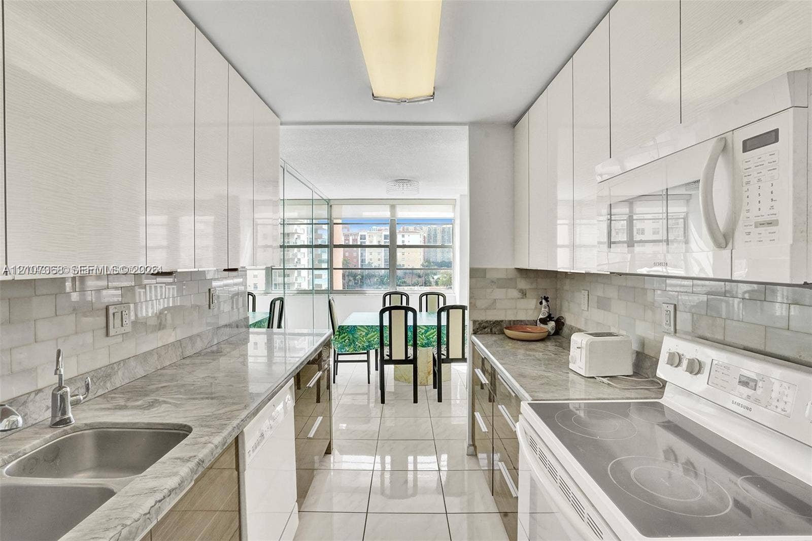 251 174th Street, #415, Sunny Isles Beach, FL 33160 Kitchen featuring gloss-finish cabinetry, stone-finish countertops, subway tile backsplash, stainless steel double-basin sink, and tile flooring